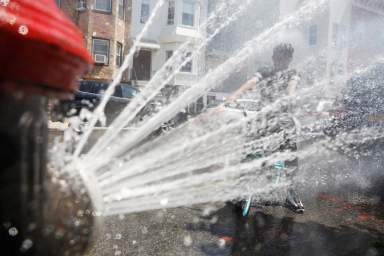 A boy on a bicycle cools off from the extreme heat from an opened fire hydrant in Brooklyn, New York